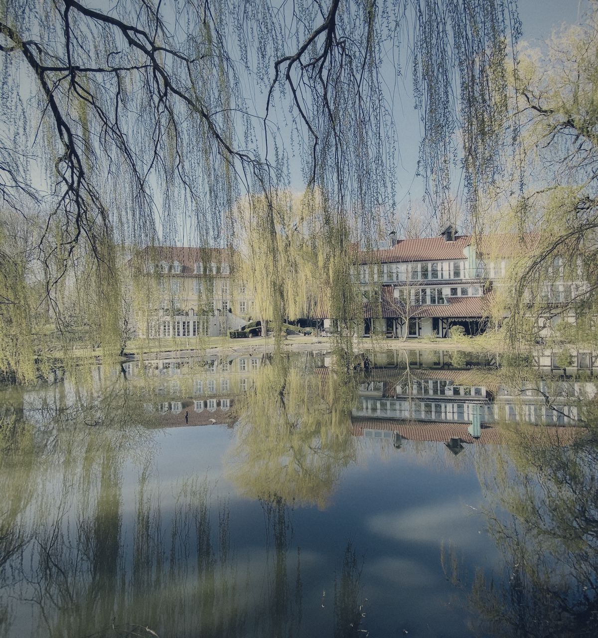 Das Amtshaus spiegelt sich im Schlossteich zwischen Trauerweiden
